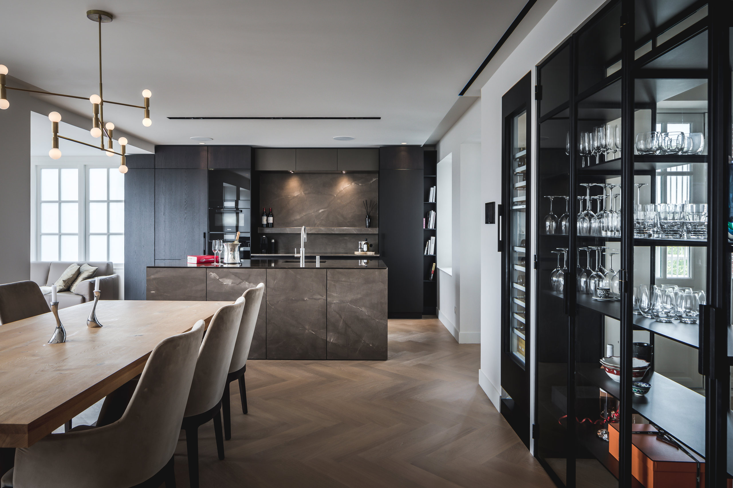 Eetkamer met eettafel, donkere keuken en glazen vitrinekasten met glaswerk