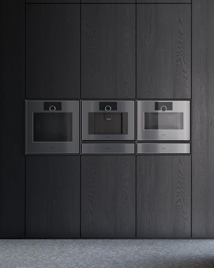 Drie Gaggenau ovens naast elkaar in een kastenwand van donker hout