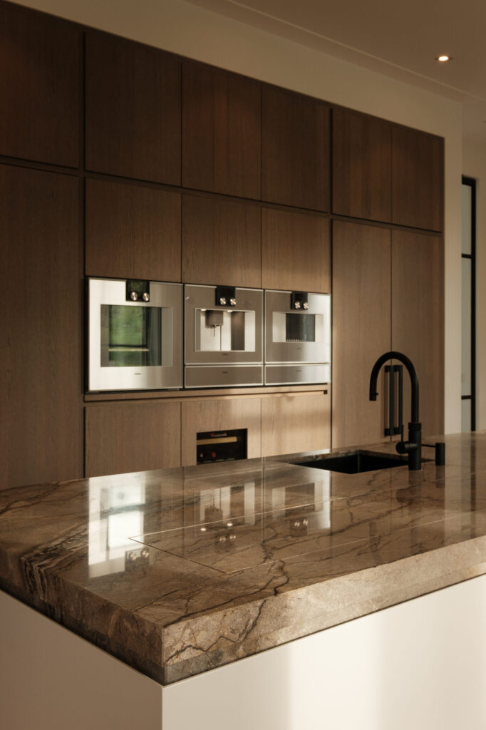 Gaggenau ovens in een houten kastenwand achter een natuurstenen werkblad in een keuken van Culimaat